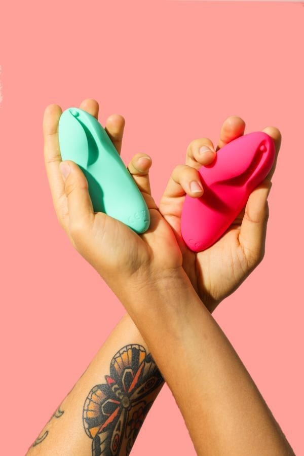 Two hands crossed, each holding the vagina-shaped oval toy 
