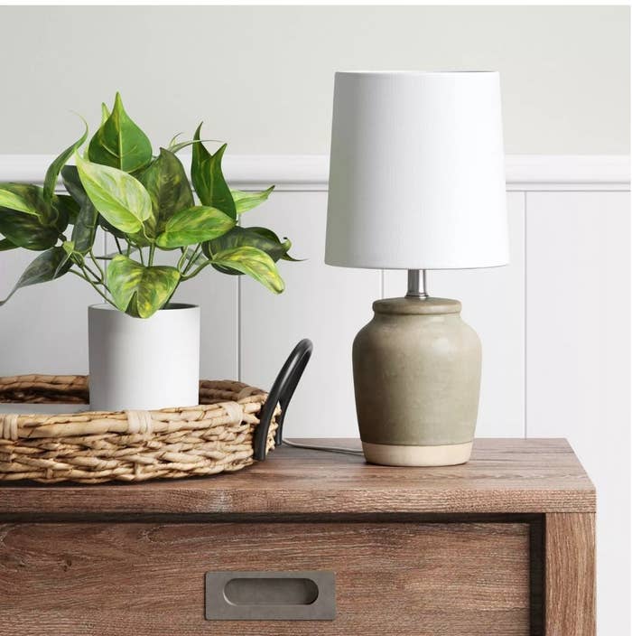 An olive and beige ceramic lamp with a white drum displayed on a wooden dresser