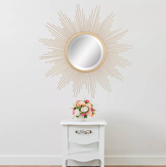 A sunburst wall mirror with an antique gold finish displayed above a dresser
