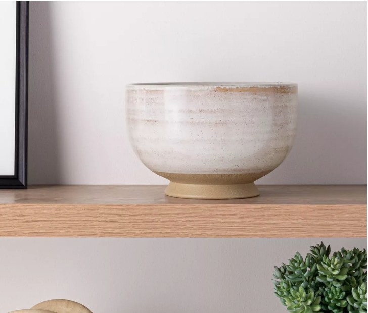 A cream, ceramic bowl displayed on a shelf