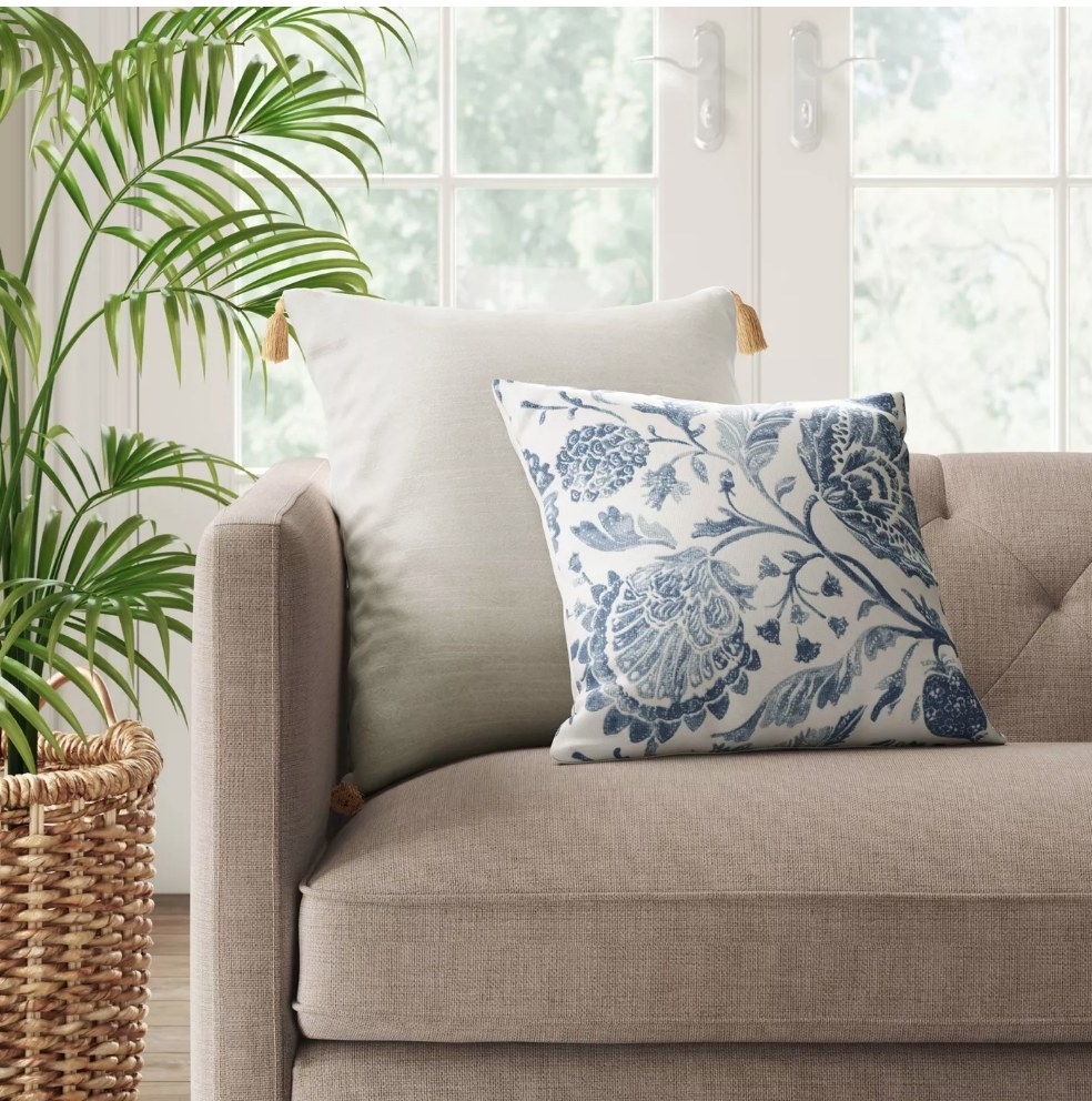 A blue and off-white floral throw pillow displayed on a couch