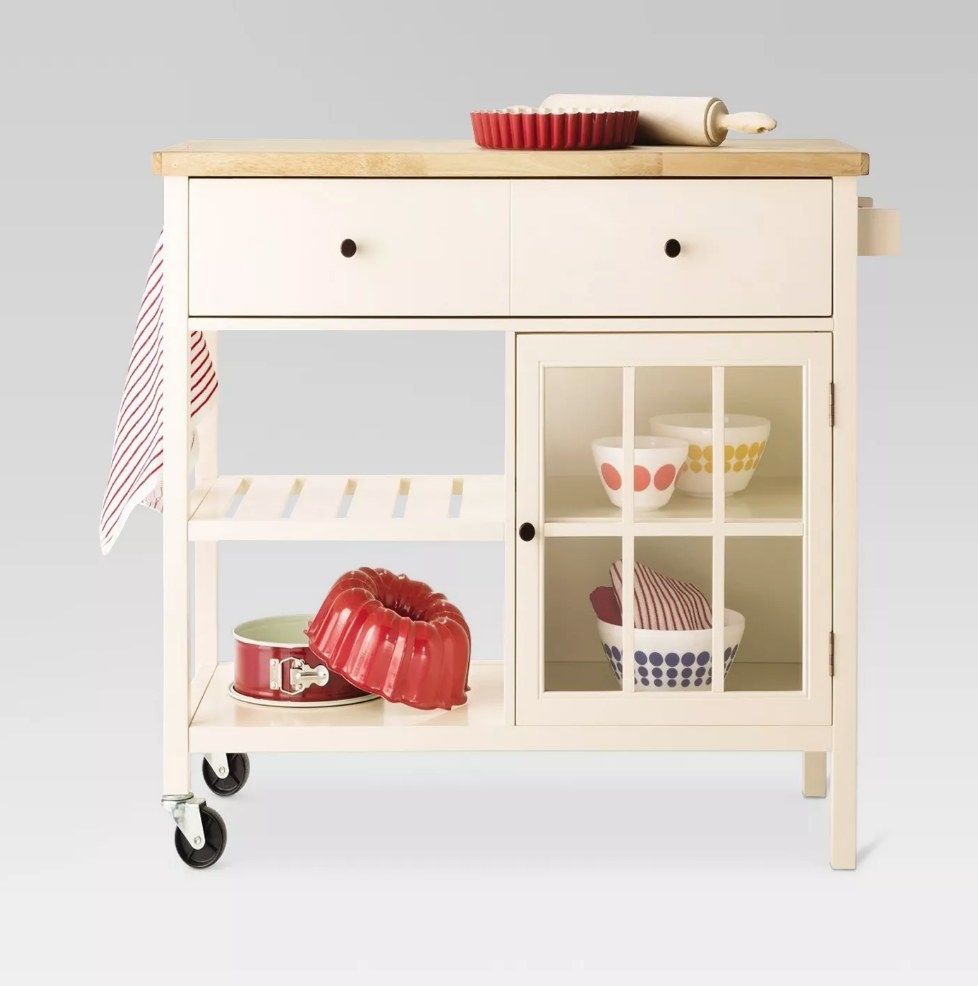 A shell-colored kitchen island with a wooden top, four shelves, one drawers, and two wheels