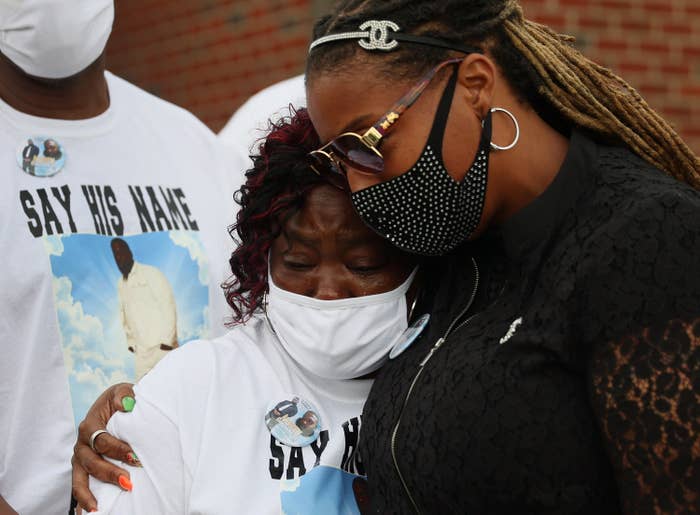 Two Black women wearing face masks hold each other