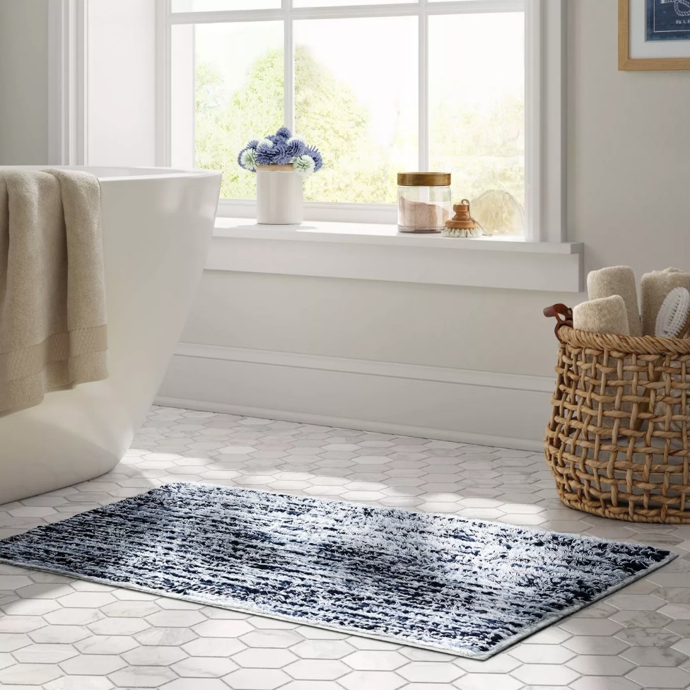 A 20&quot; x 32&quot;, blue and white striped bath rug on the floor in a bathroom