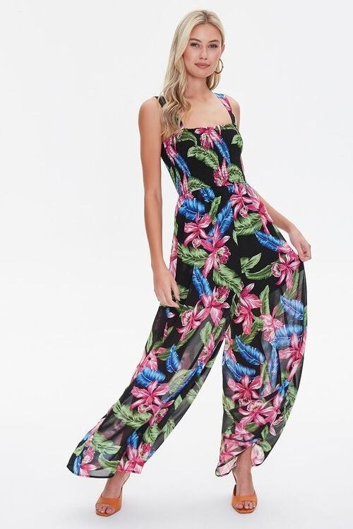 Model wearing sleeveless black jumpsuit with blue, pink, and green tropical print