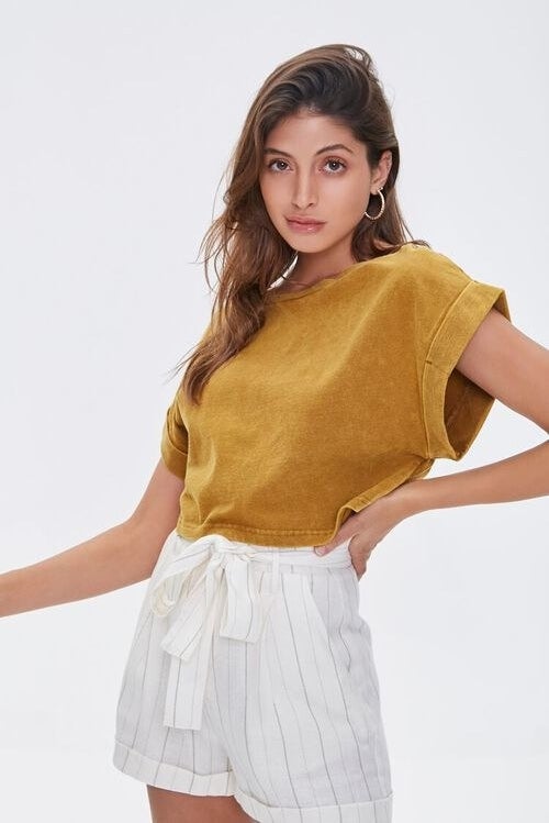 Model wearing mustard yellow tee with cuff sleeves, stops at the waist 
