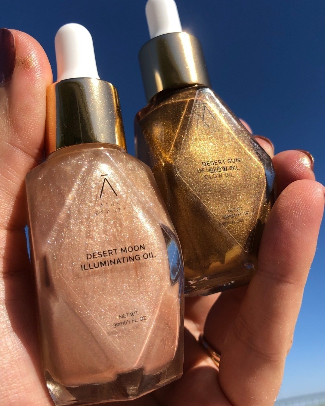 A person holding up two bottles of the shimmer oil; the sun is reflecting off the diamond dust