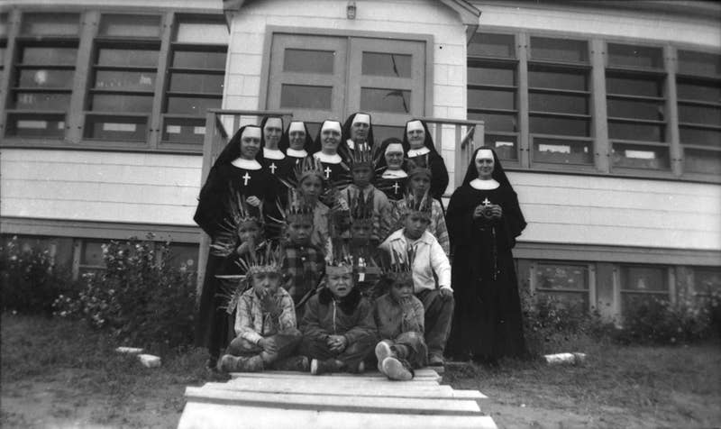 A group of nuns stand in front of sitting Indigenous children