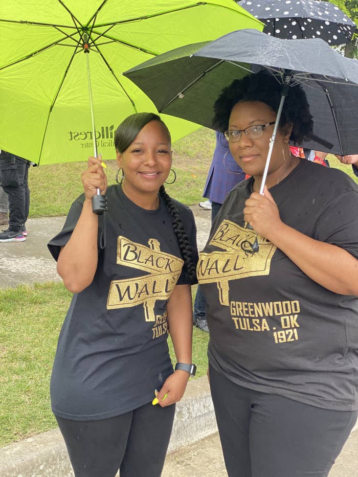 Two women stand together under umbrellas with T-shirts commemorating Black Wall Street