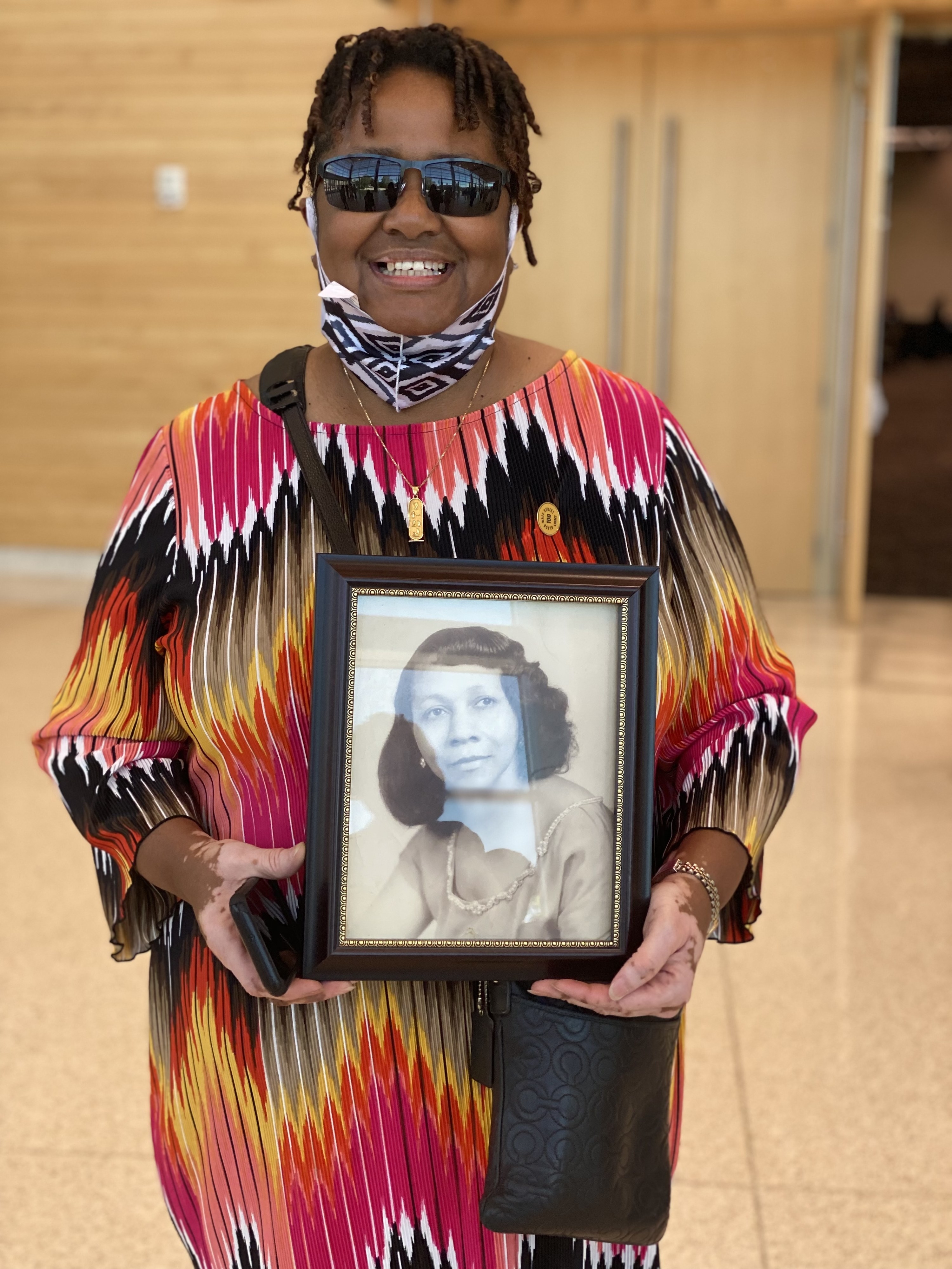 A smiling Cherri Lewis stands while holding a framed photo of her grandmother