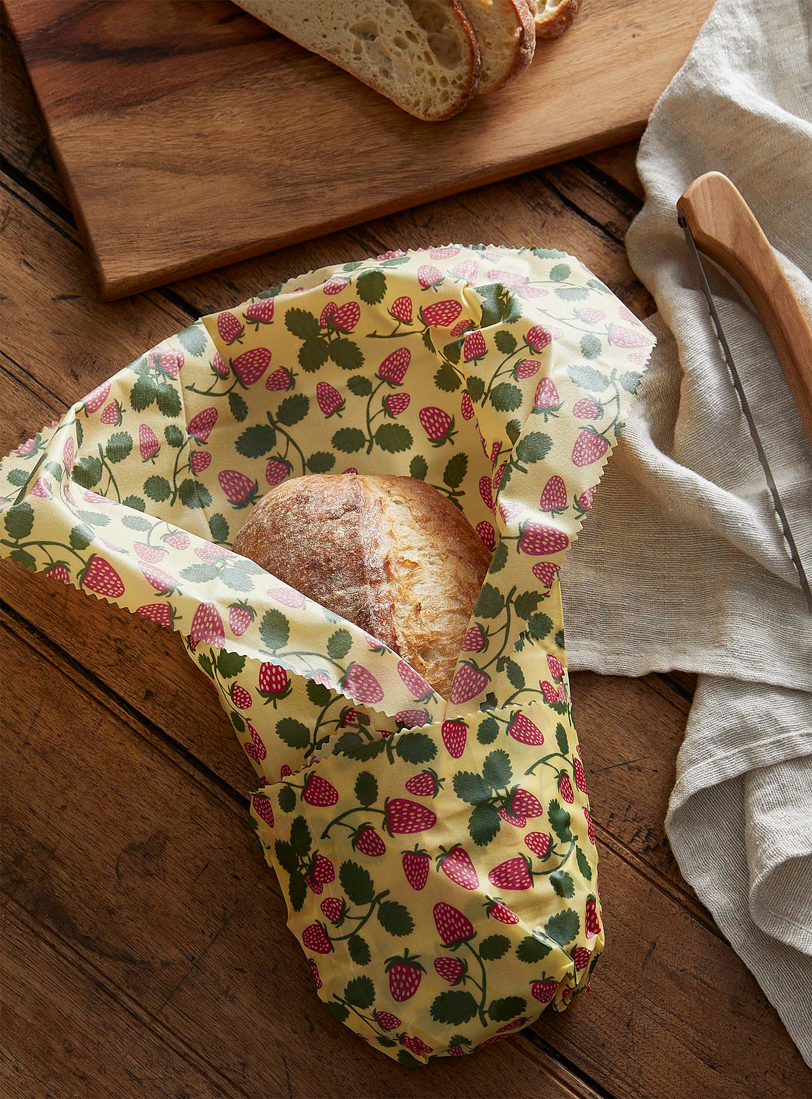 A large beeswax wrap in a strawberry print wrapped around a loaf of bread