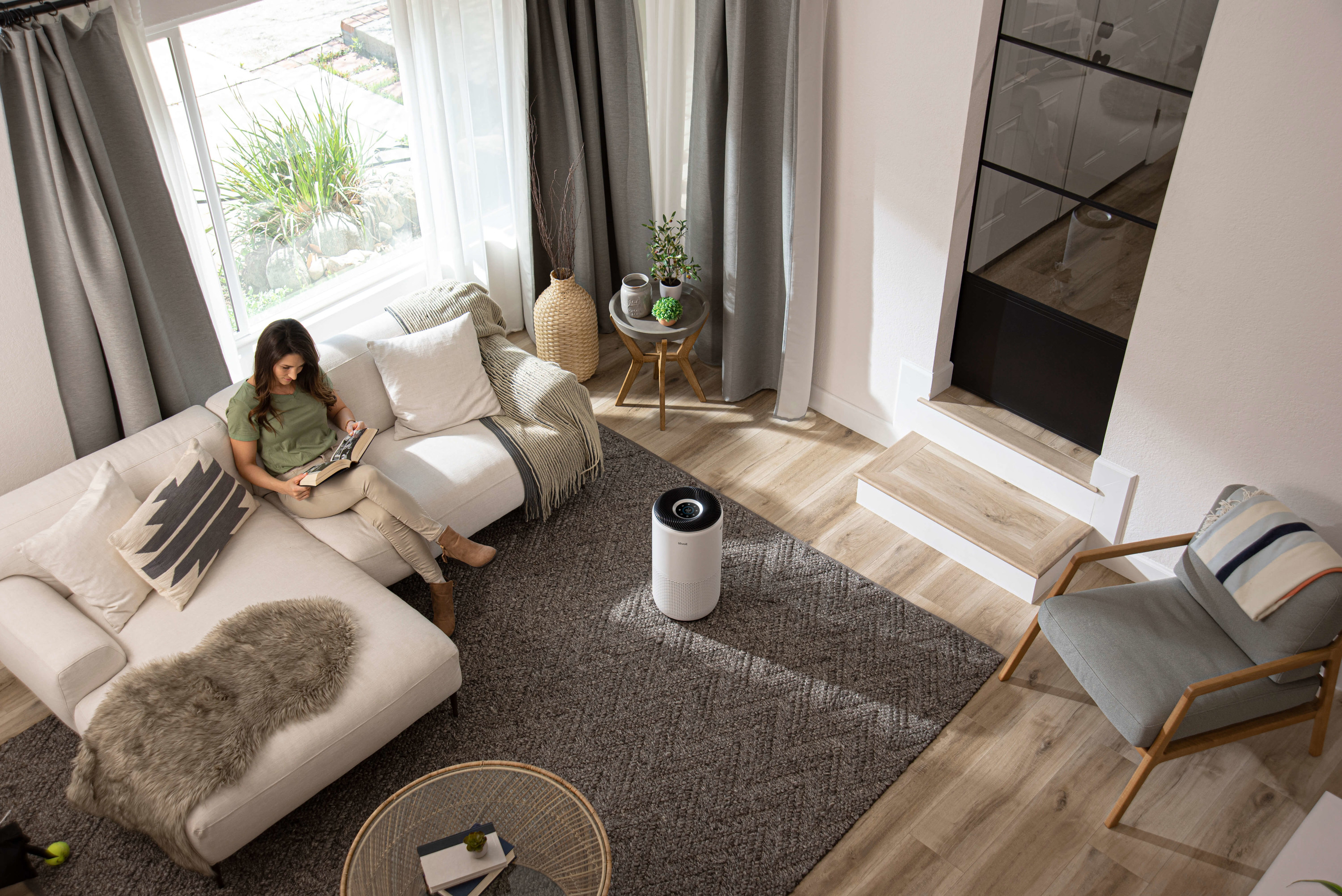 woman sitting on couch while air purifier cleans the air in the room