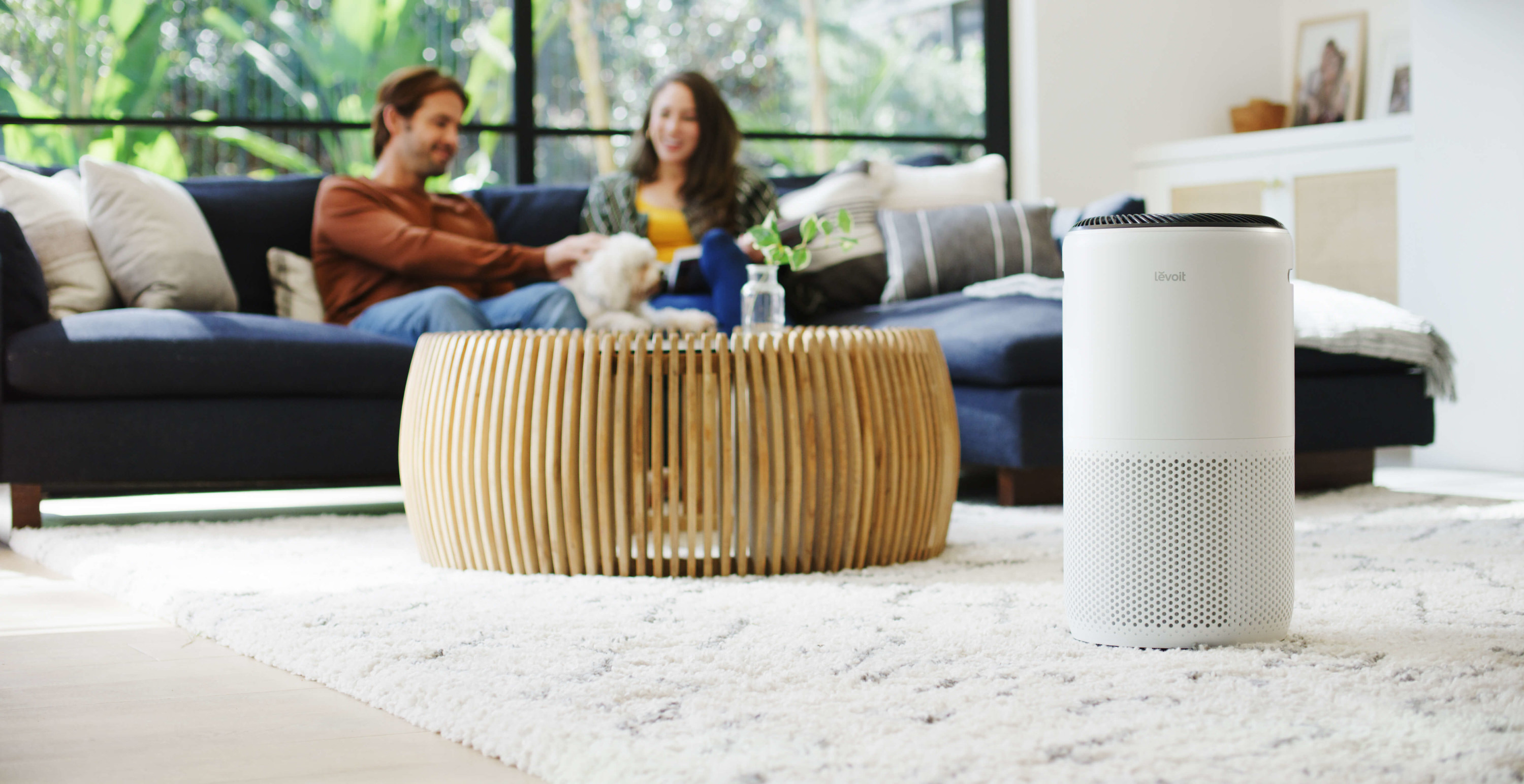 Two people relaxing on the couch as the air purifier runs nearby