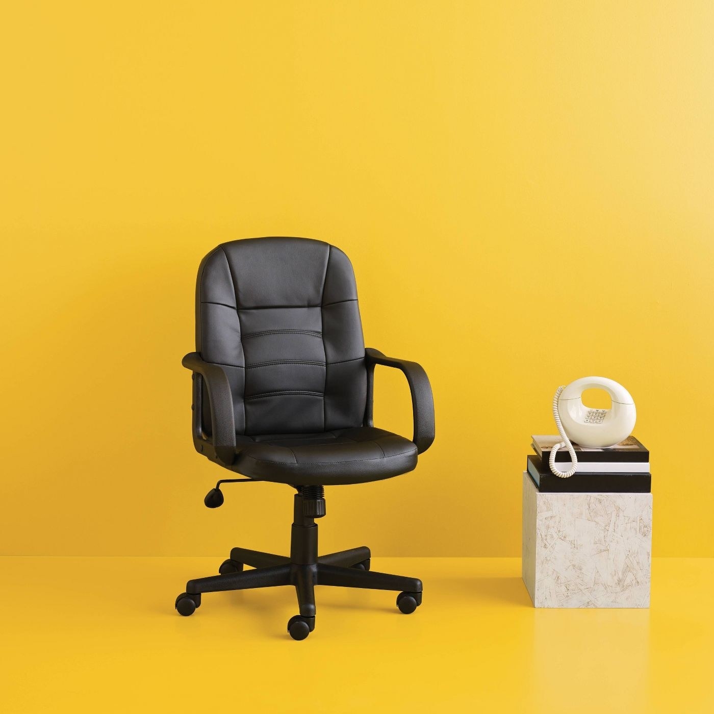 A black leather swivel office chair on a yellow backdrop