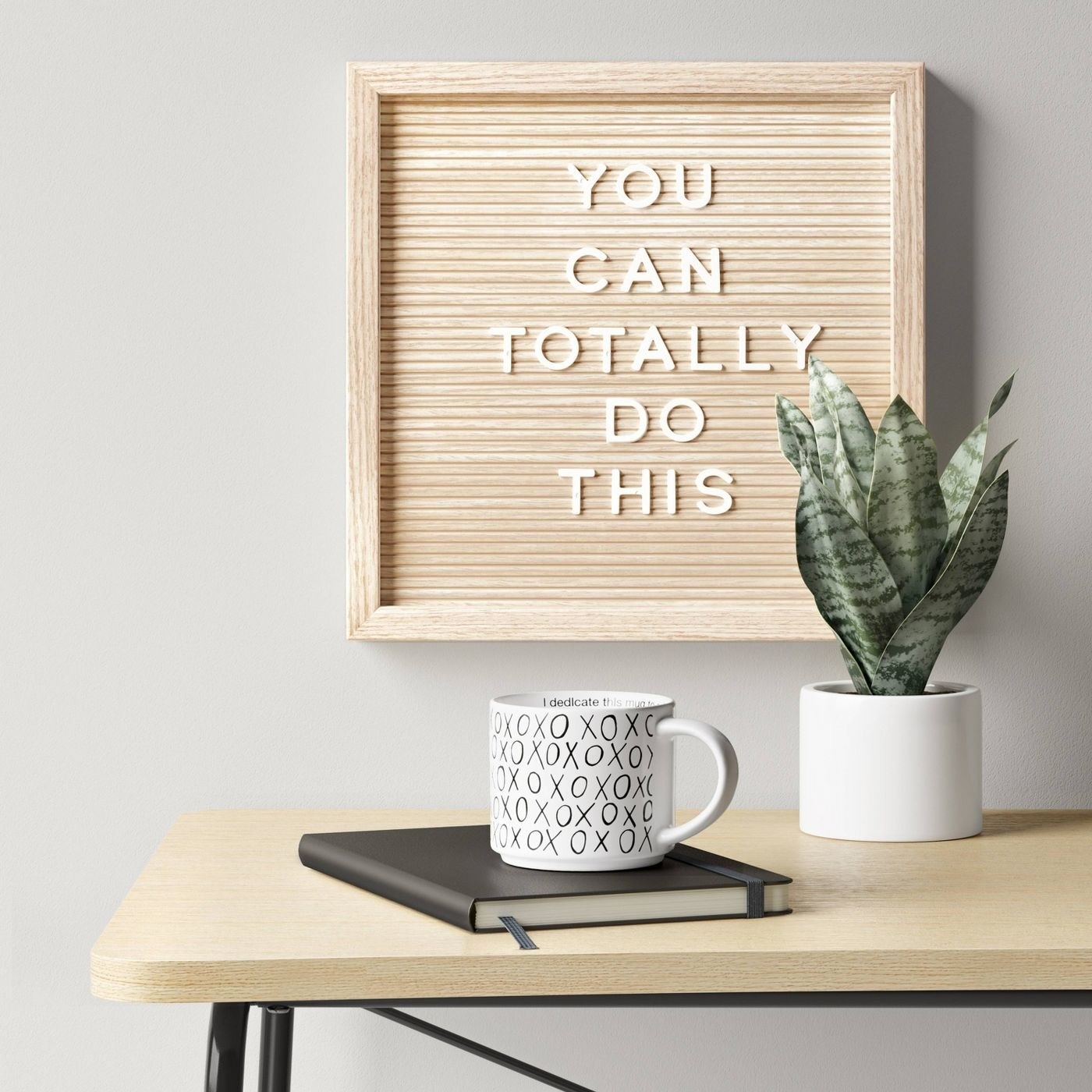 A square faux wood letter board hanging above a desk