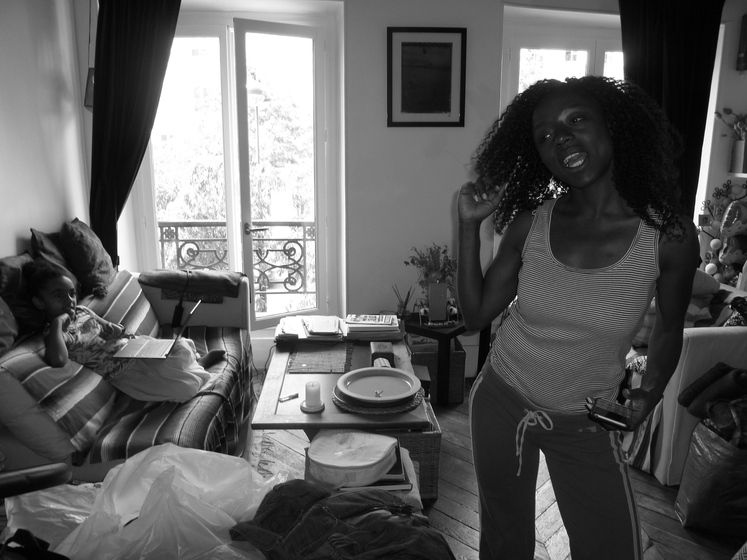 A woman stands in her apartment while her young daughter watches