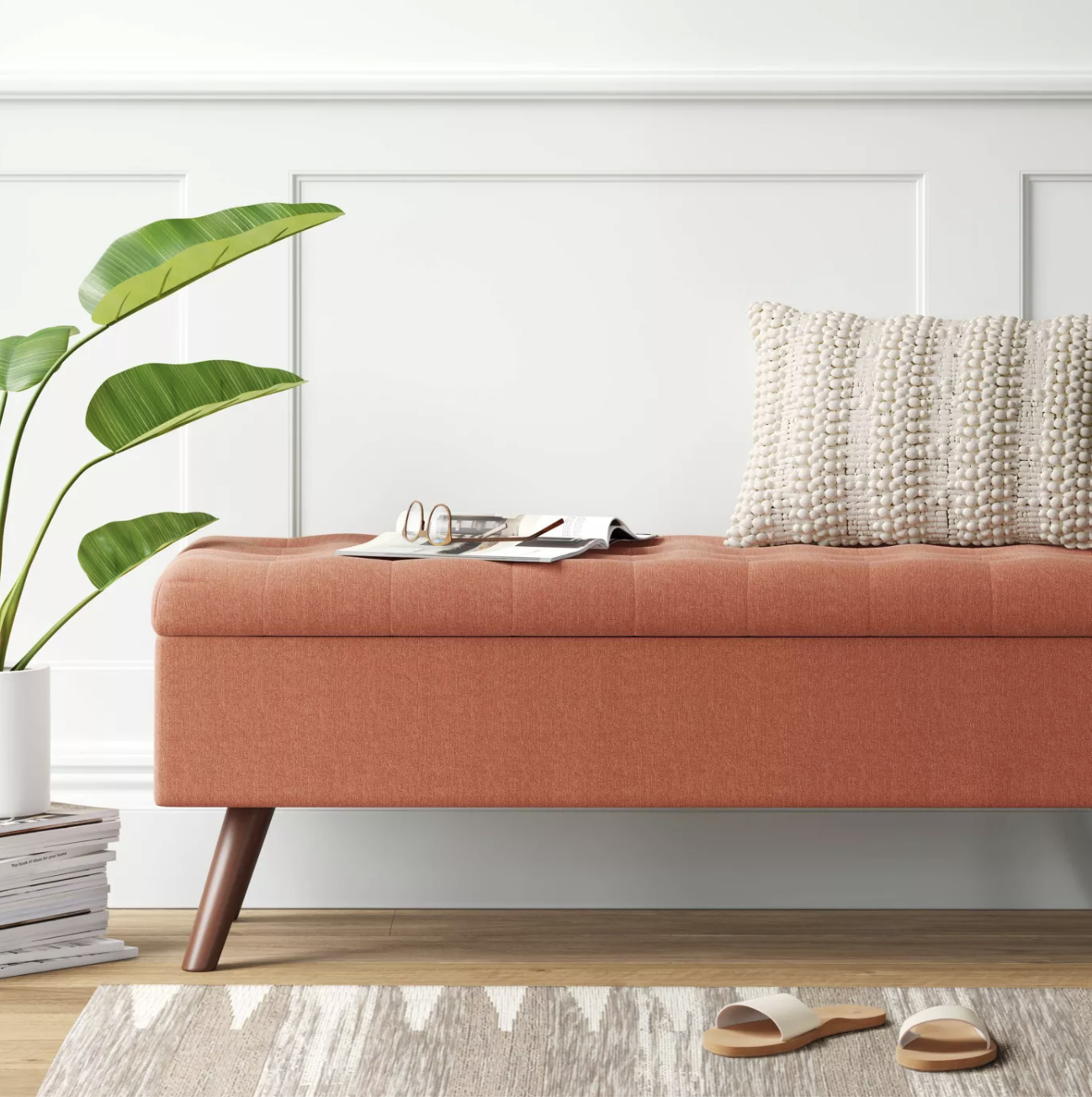 An orange, tufted storage bench with four brown wooden legs