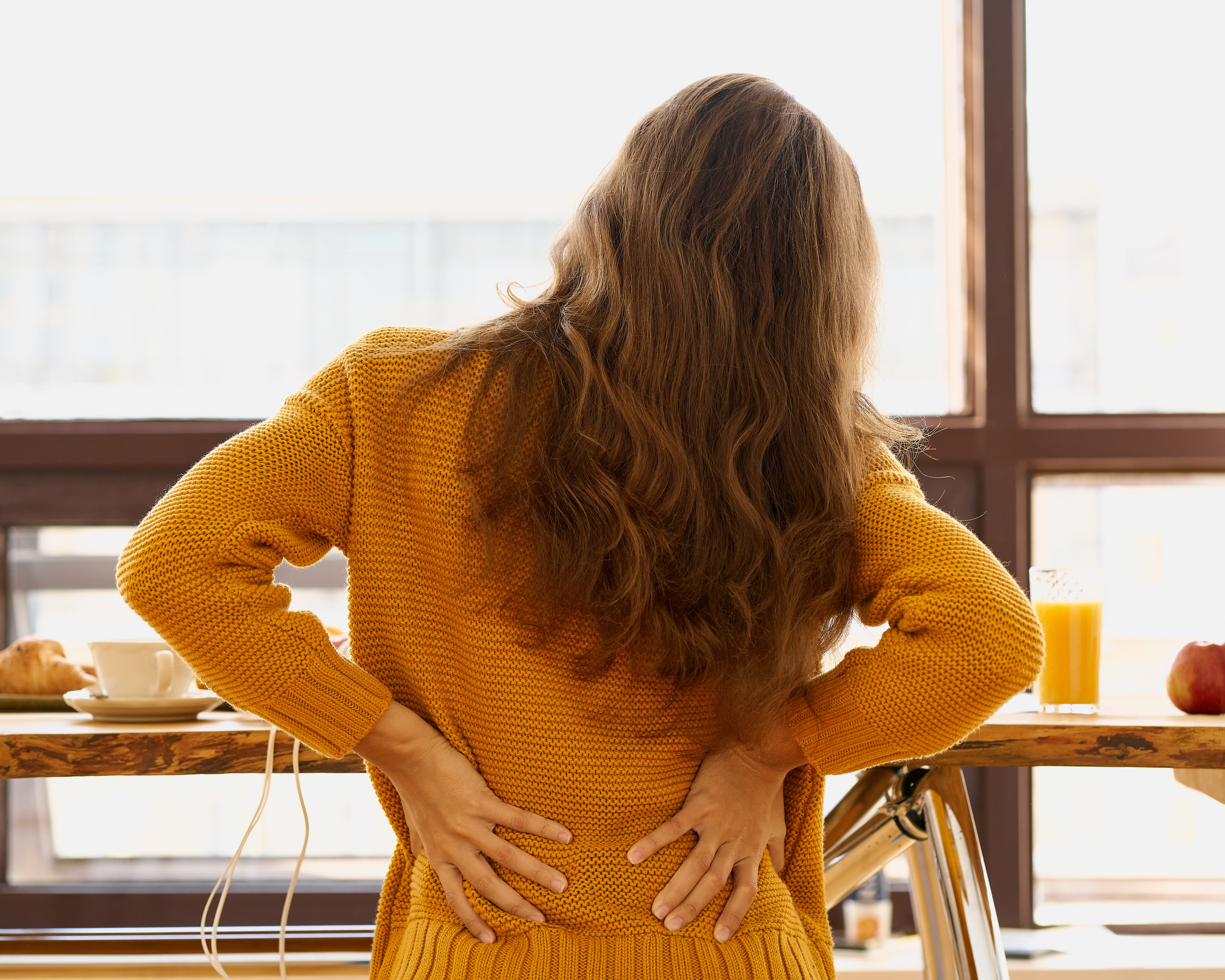 Photo of a woman in a yellow sweater stretching her back