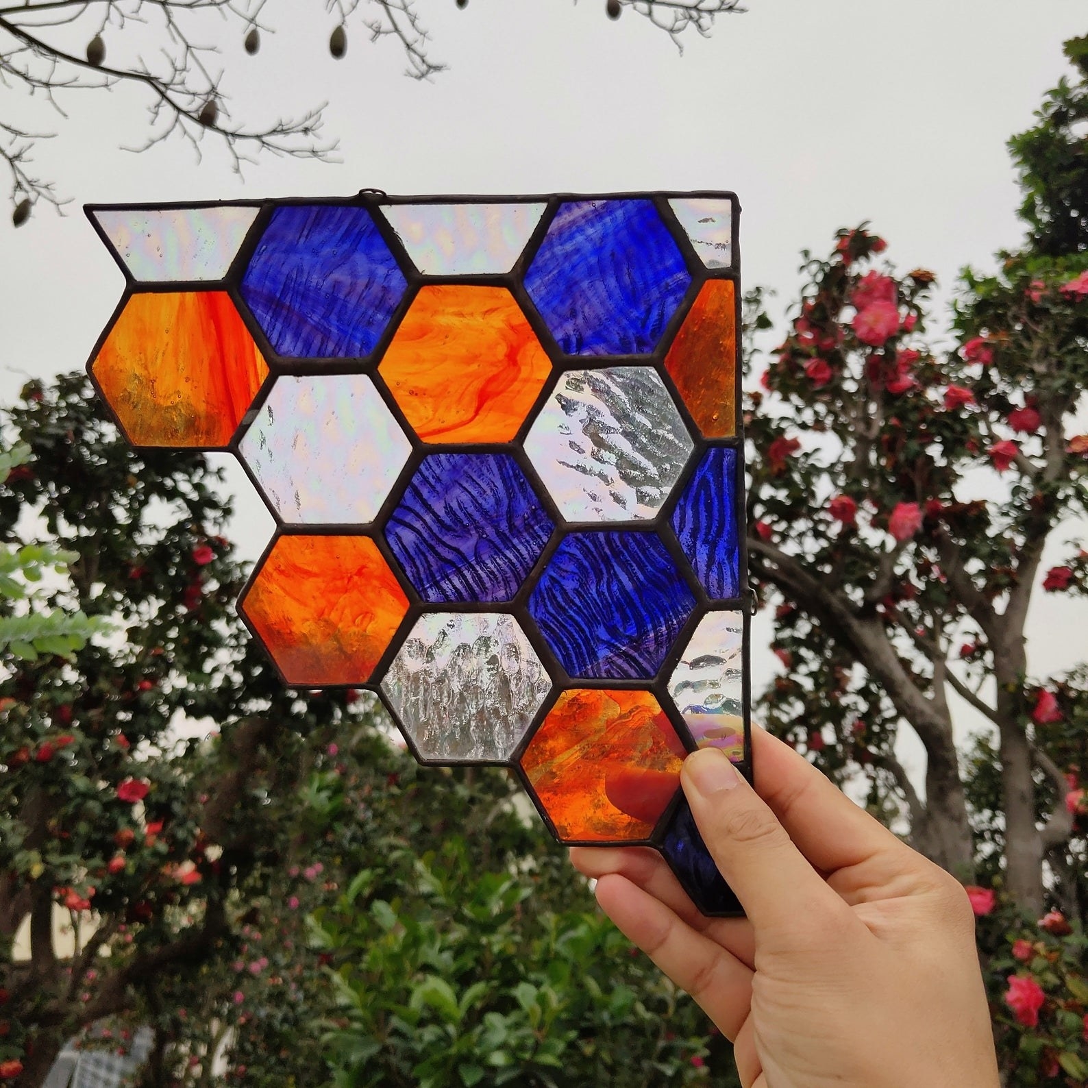 a hand holds the stained glass honeycomb sun catcher up to the sky