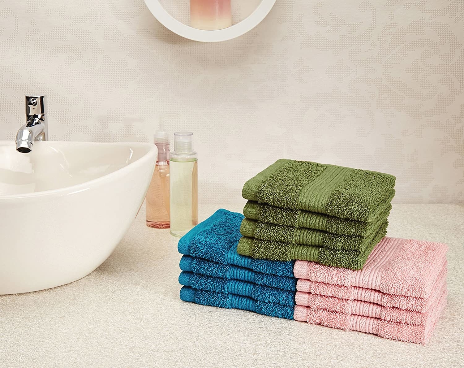 Pink, blue, and green hand towels stacked up next to a washbasin.