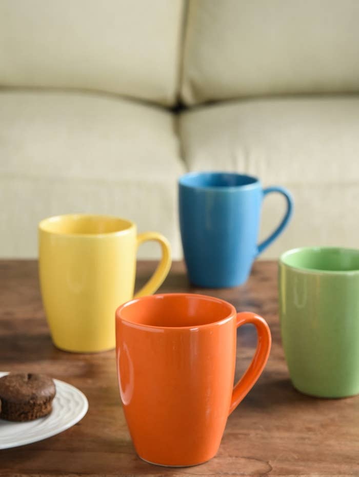 Orange, yellow, blue, and green mugs kept next to a plate of muffins.