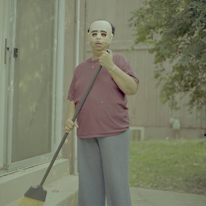 woman holds a broom while wearing a plastic mask