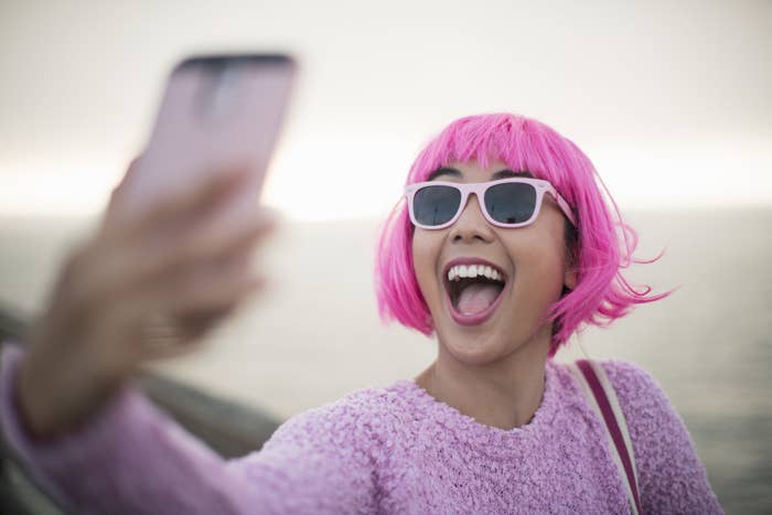 A woman with pink hair takes a selfie.