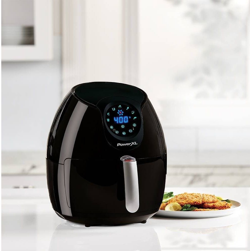 A black air fryer on a kitchen counter next to a plate of food