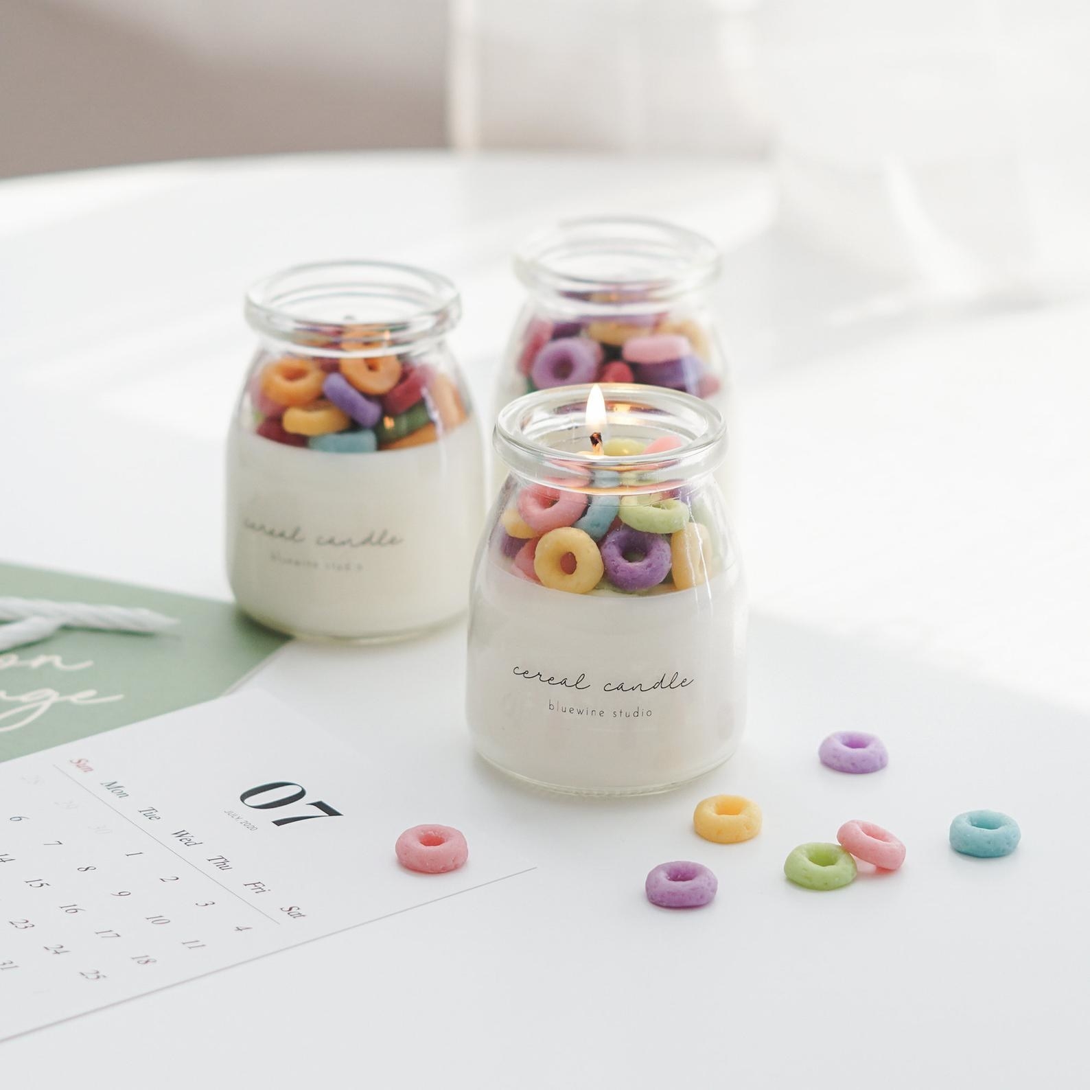 A small milk jar-shaped glass candle with wax rainbow "cereal" pieces on the top to look like Fruit Loops