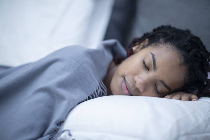 A woman covered by a blue blanket, sleeps in bed.