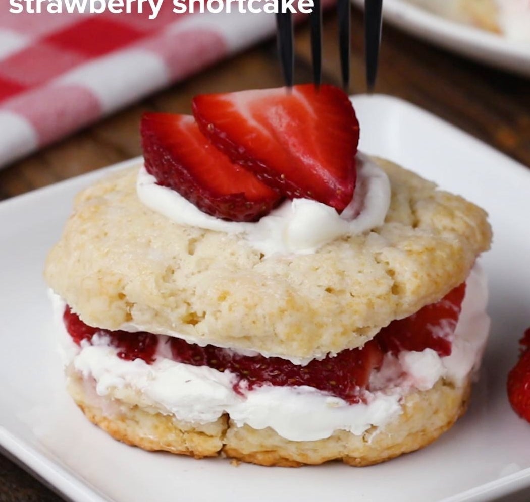 A slice of strawberry shortcake with fresh strawberry topping.
