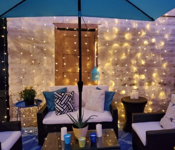 A reviewer showing how they strung the fairy light curtain against their house to create a twinkling waterfall effect on their patio 