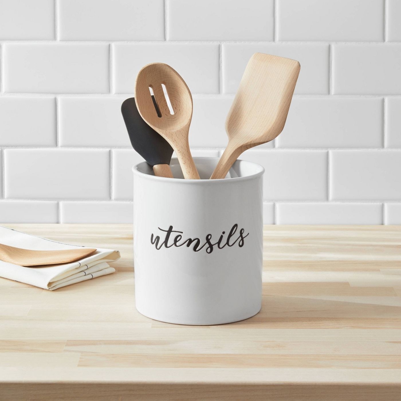 white utensil holder with "utensils" engraved on the front, holding wooden utensils