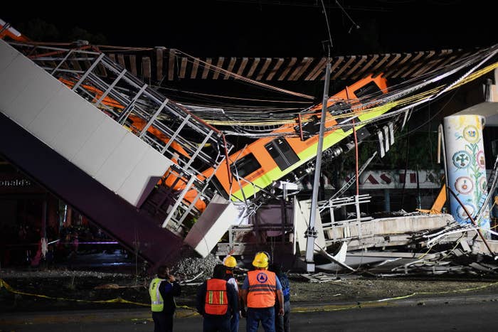 Rescue workers stand in front of the collapsed elevated train under an overpass