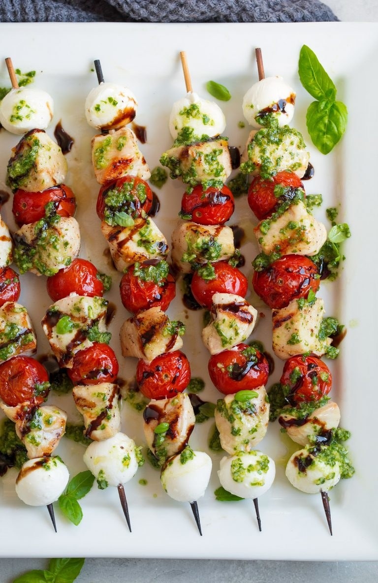 A serving tray topped with Caprese grilled chicken skewers and pesto.