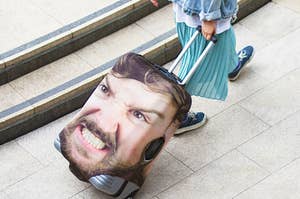 Person pulling suitcase with a personalized image of their scowling face on it