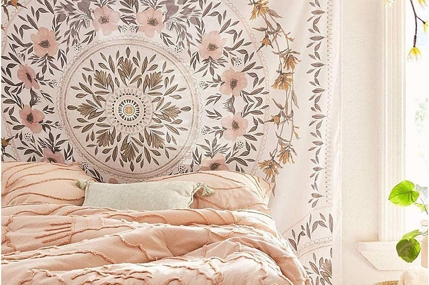 Large white tapestry with pink, green, and brown flowers in leaves in a circular pattern on the tapestry on a wall in a bedroom