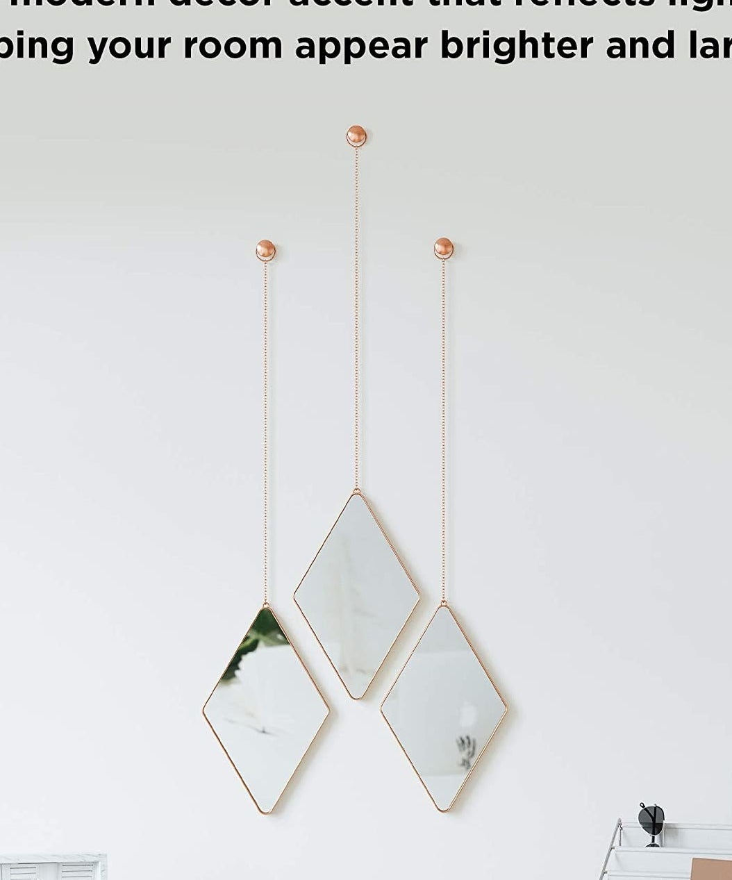 three diamond shaped mirrors hanging from dainty chains on a wall 