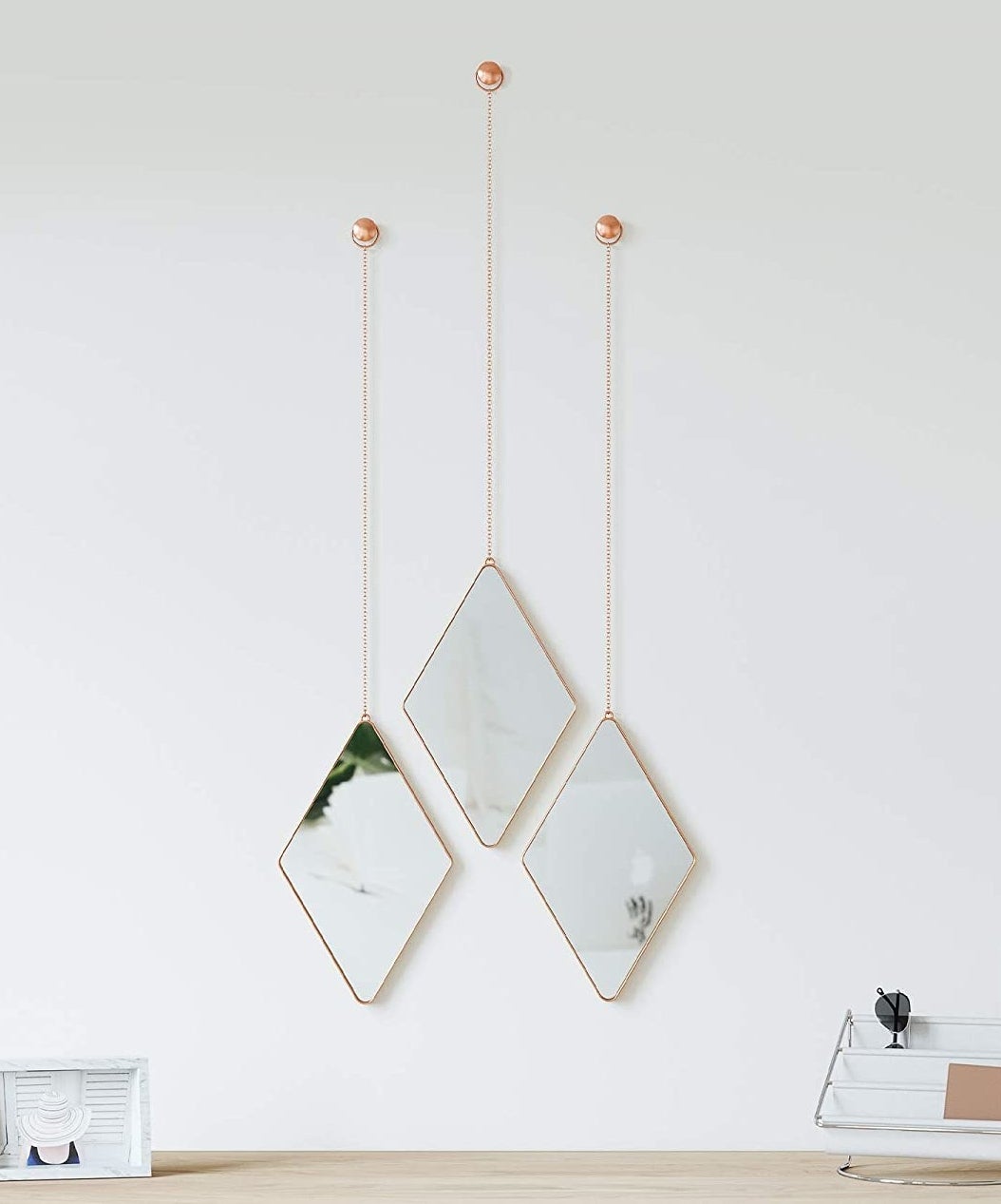 three diamond shaped mirrors hanging from dainty chains on a wall 