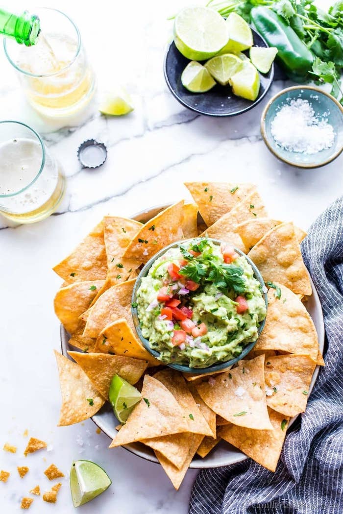 A bowl of guacamole with tortilla chips and lime wedges. 