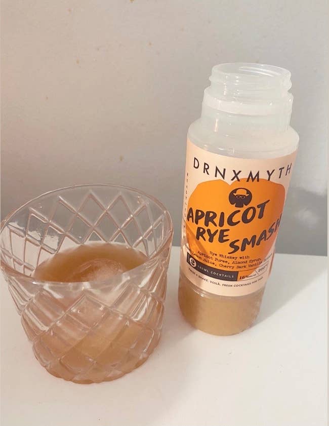 A bottle of Apricot Rye Smash cocktail next to a whiskey glass full of the cocktail 