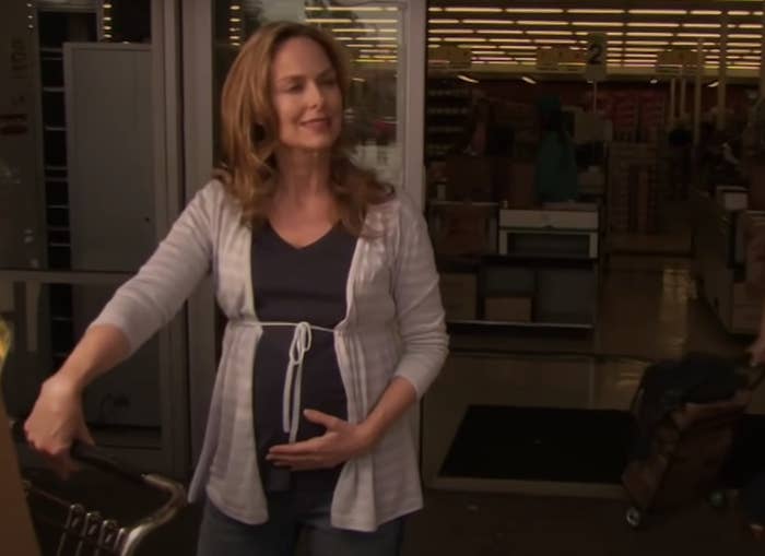 Jan holds her baby bump while standing outside a supermarket