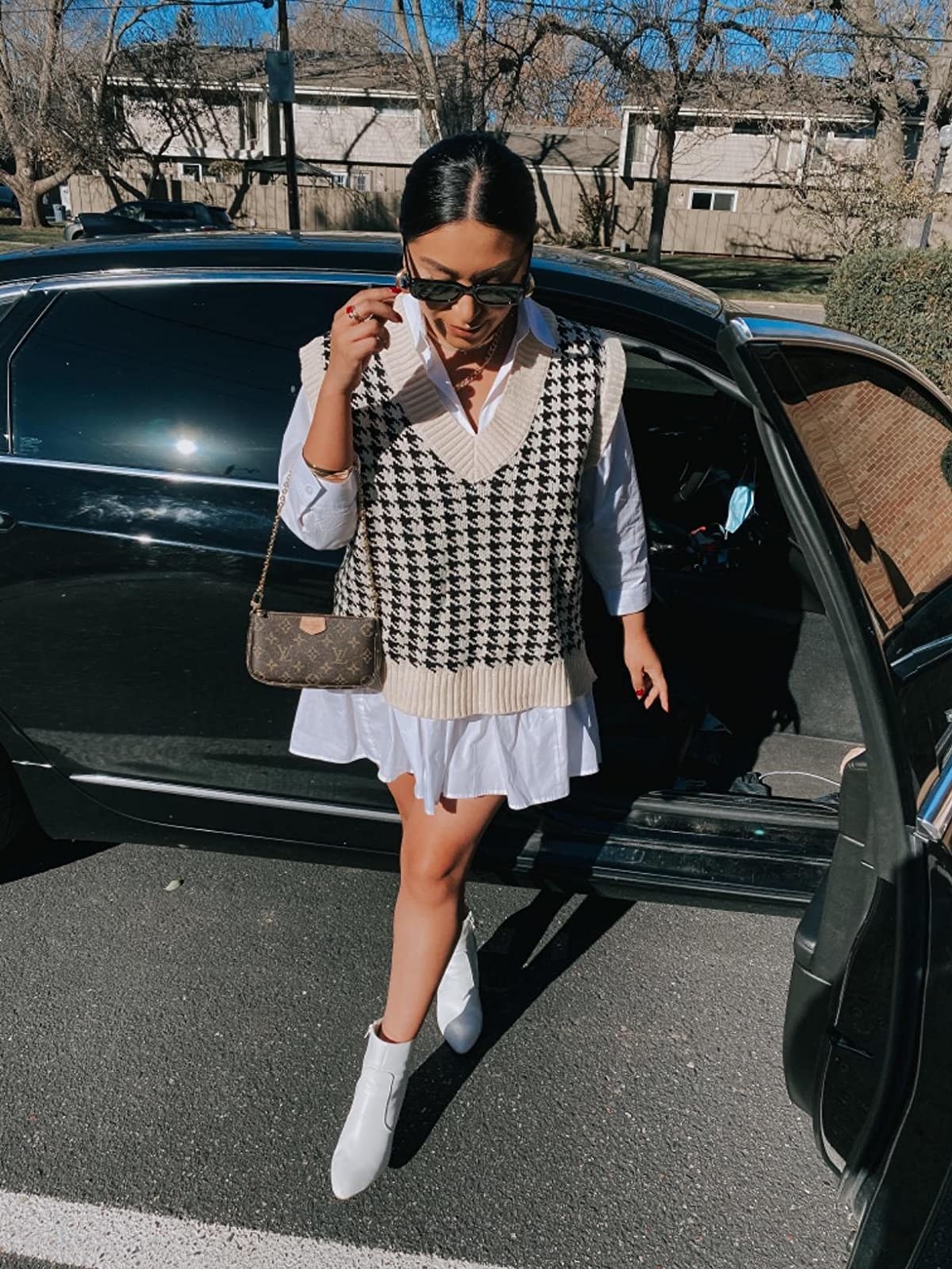 reviewer steps out of a car wearing the oversized houndstooth knitted vest over a white shirt-dress