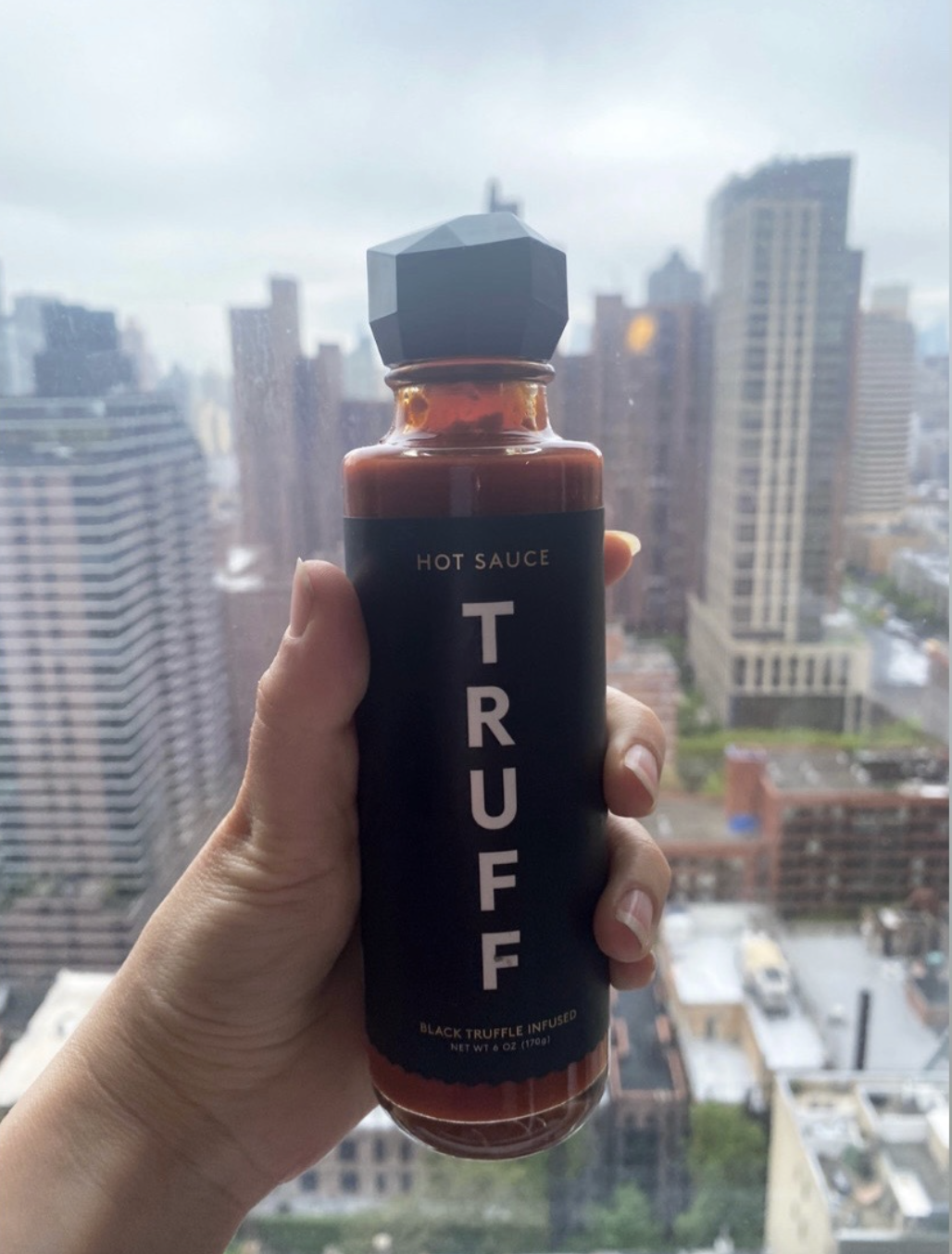 Editor holding up bottle of red Truff sauce in front of skyline window 