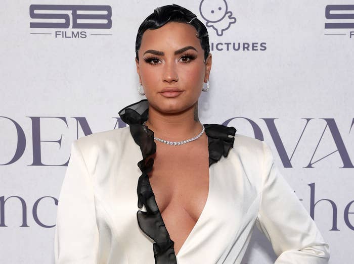 Demi poses in a white, deep V-neck silk shirt at the premiere of her documentary