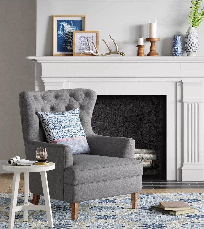A dark gray, upholstered, tufted accent chair with a throw pillow displayed next to a side table