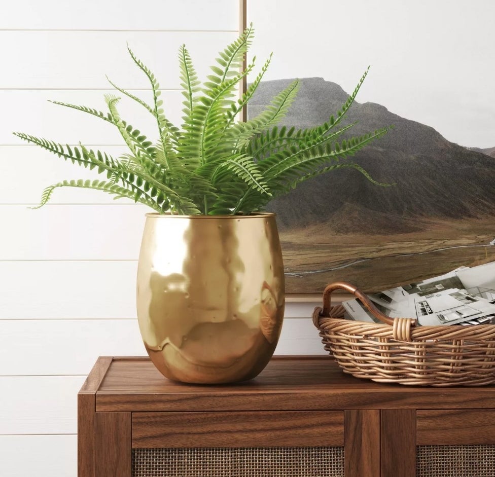 A 9.6&quot; x 9.6, gold metal planter filled with greenery and displayed on a dresser