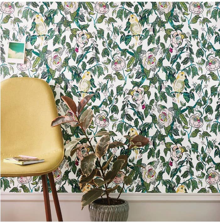 A canary, floral peel &amp;amp; stick wallpaper on a wall behind a planter and a yellow accent chair