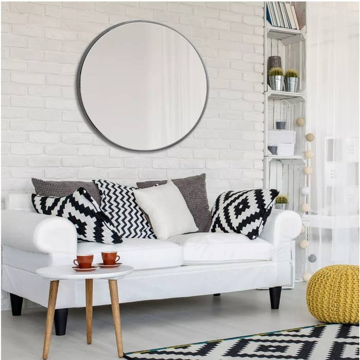 A 28&quot; round wall mirror in black hanging above a white couch with black and white accent pillows