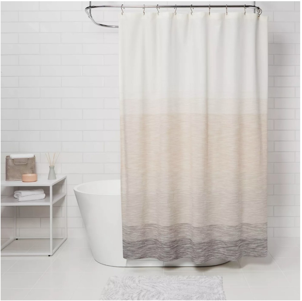 A beige ombre shower curtain hanging on a rod above a bathtub in a bathroom